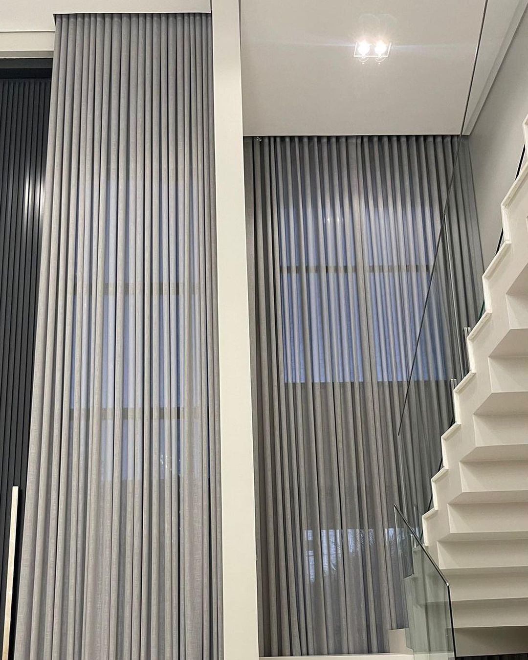 Cortinas cinza verticais em pé direito duplo com escada moderna