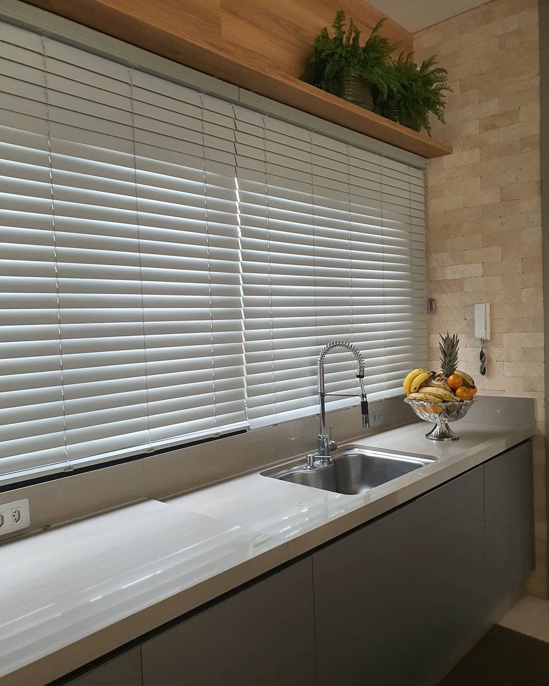 Persiana horizontal branca em área de serviço com parede de tijolinhos e plantas