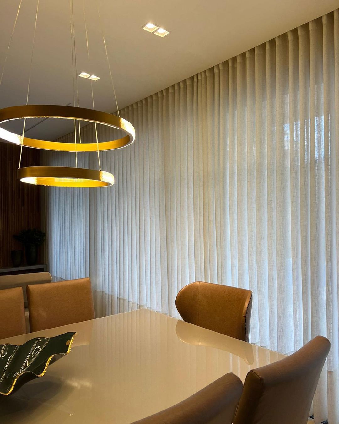 Cortinas brancas verticais em sala de jantar com lustre circular dourado