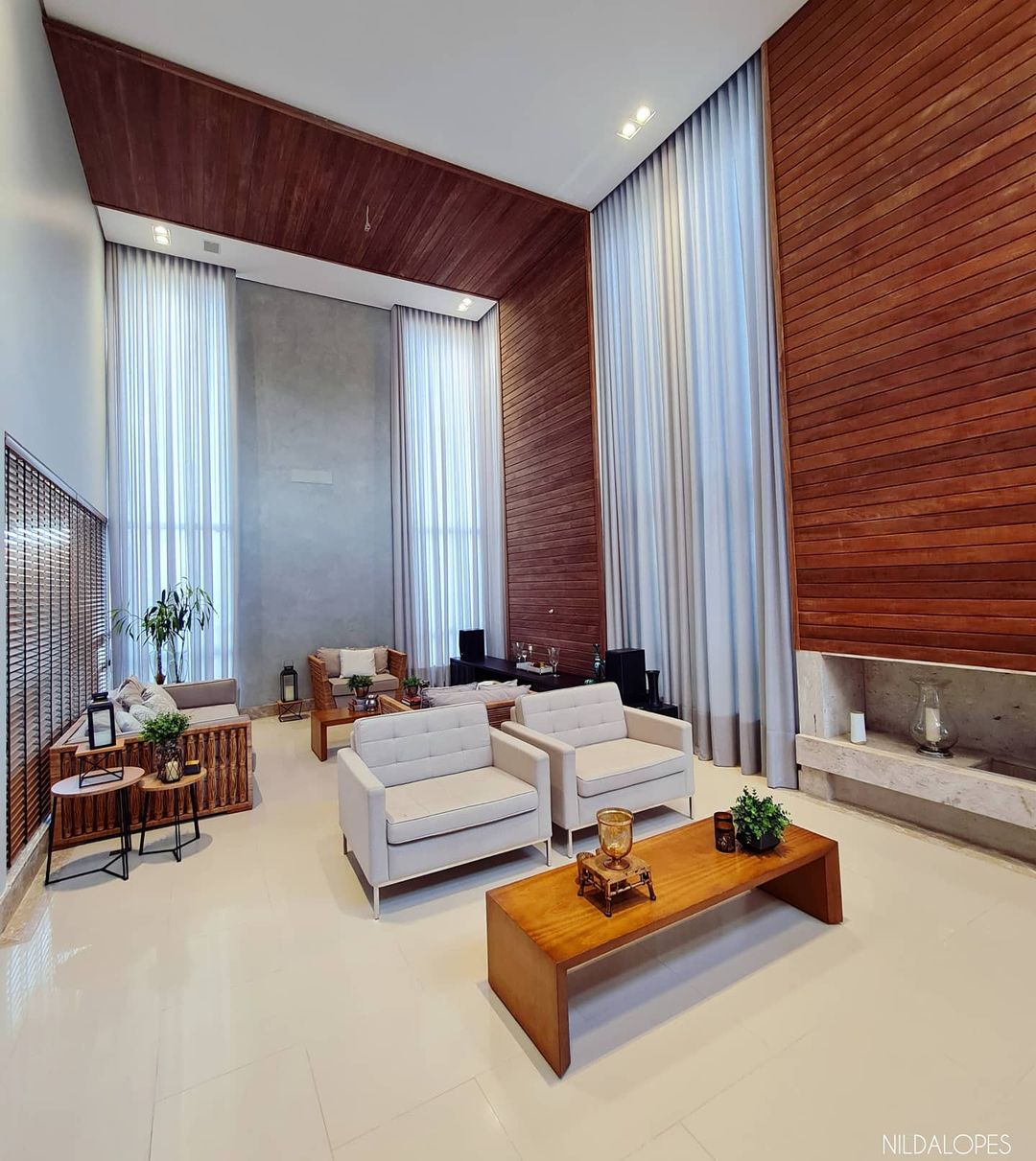 Cortinas brancas em ambiente de pé direito duplo com revestimento de madeira