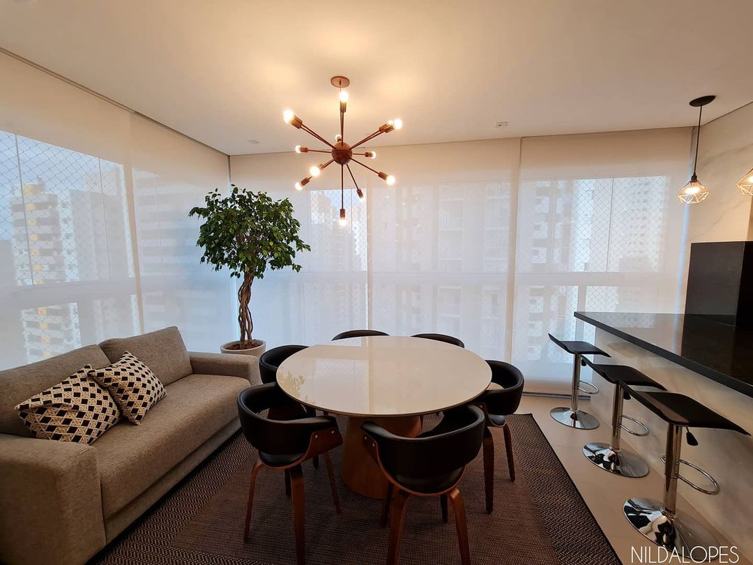 Persianas rolô translúcidas em sala integrada com mesa redonda e lustre sputnik