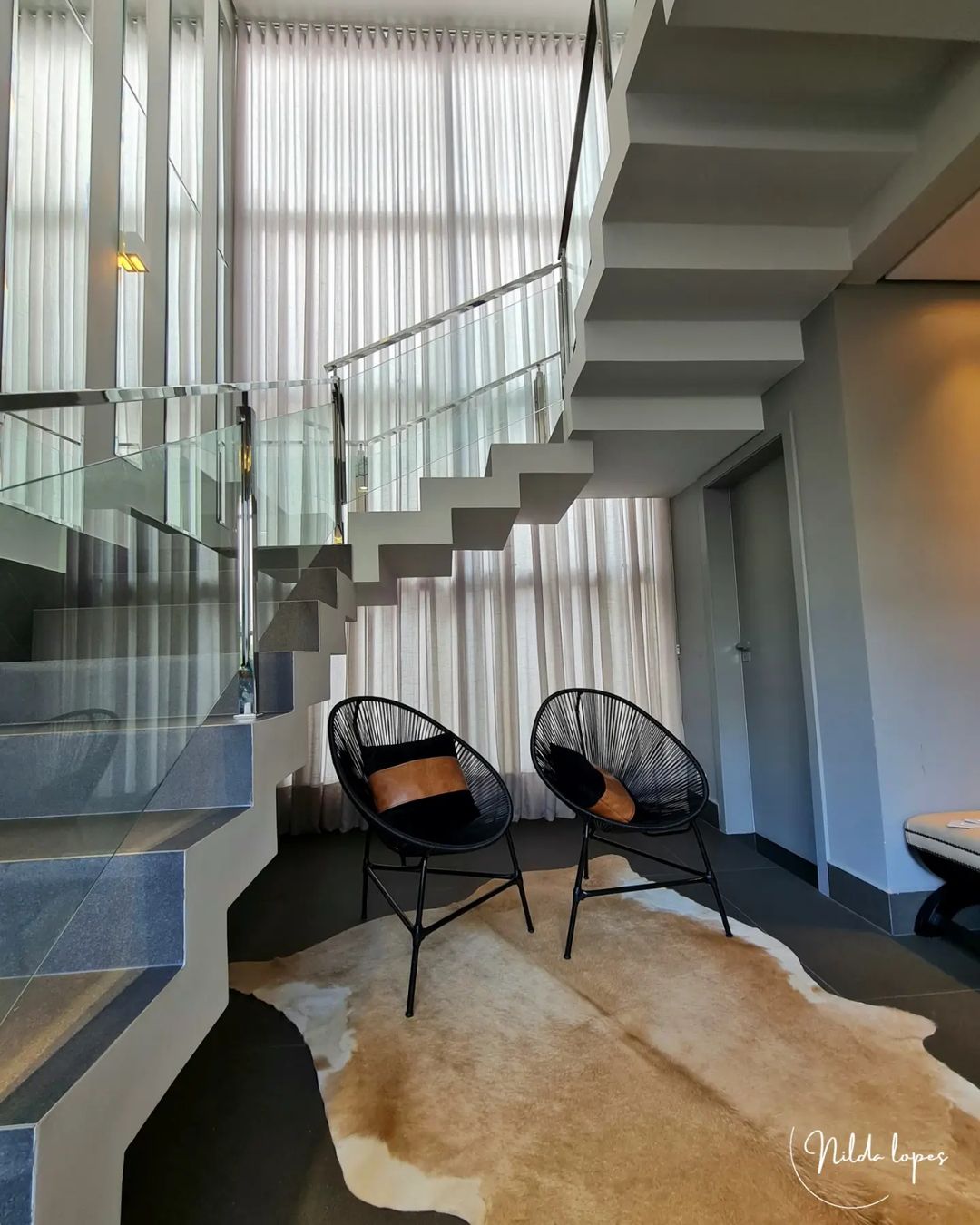 Cortinas brancas em escada moderna com poltronas pretas
