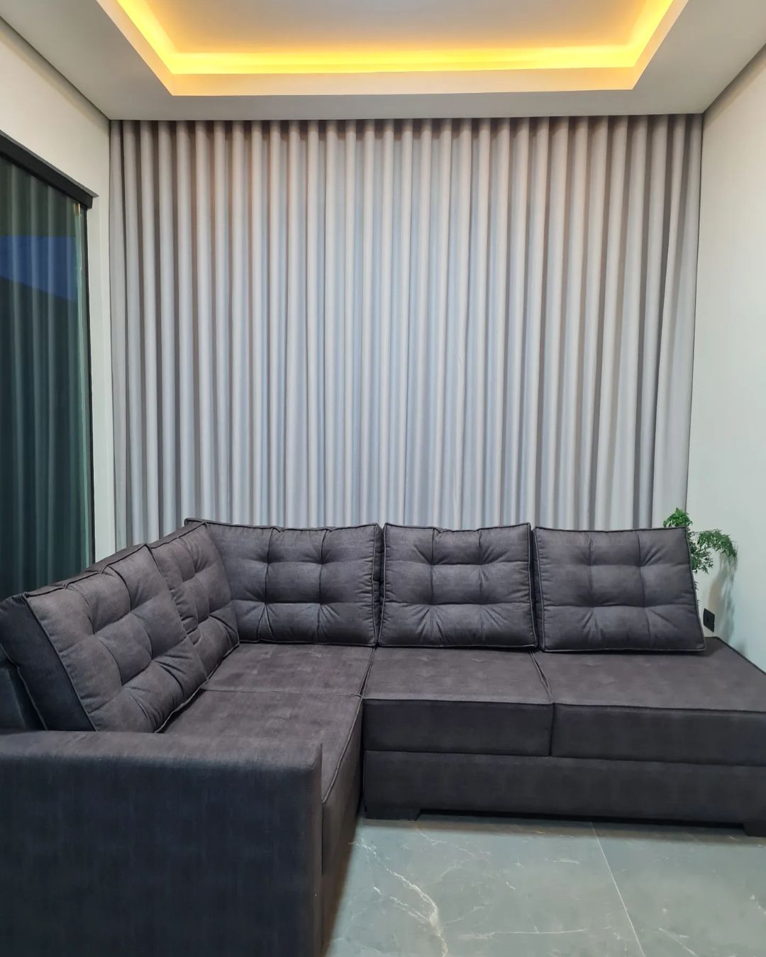 Cortinas cinza em sala com sofá em L e iluminação cênica