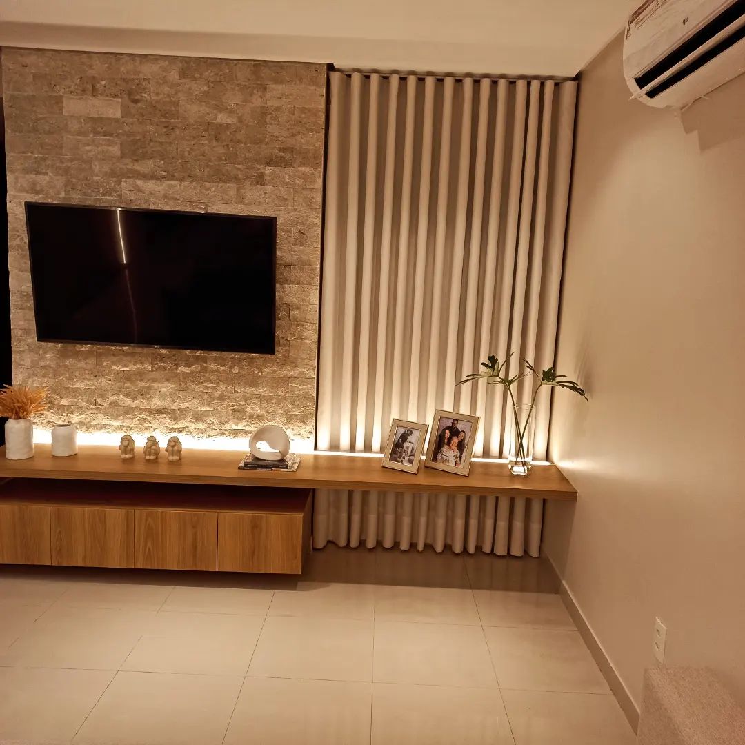Cortinas bege em sala de TV com painel de pedra e iluminação LED