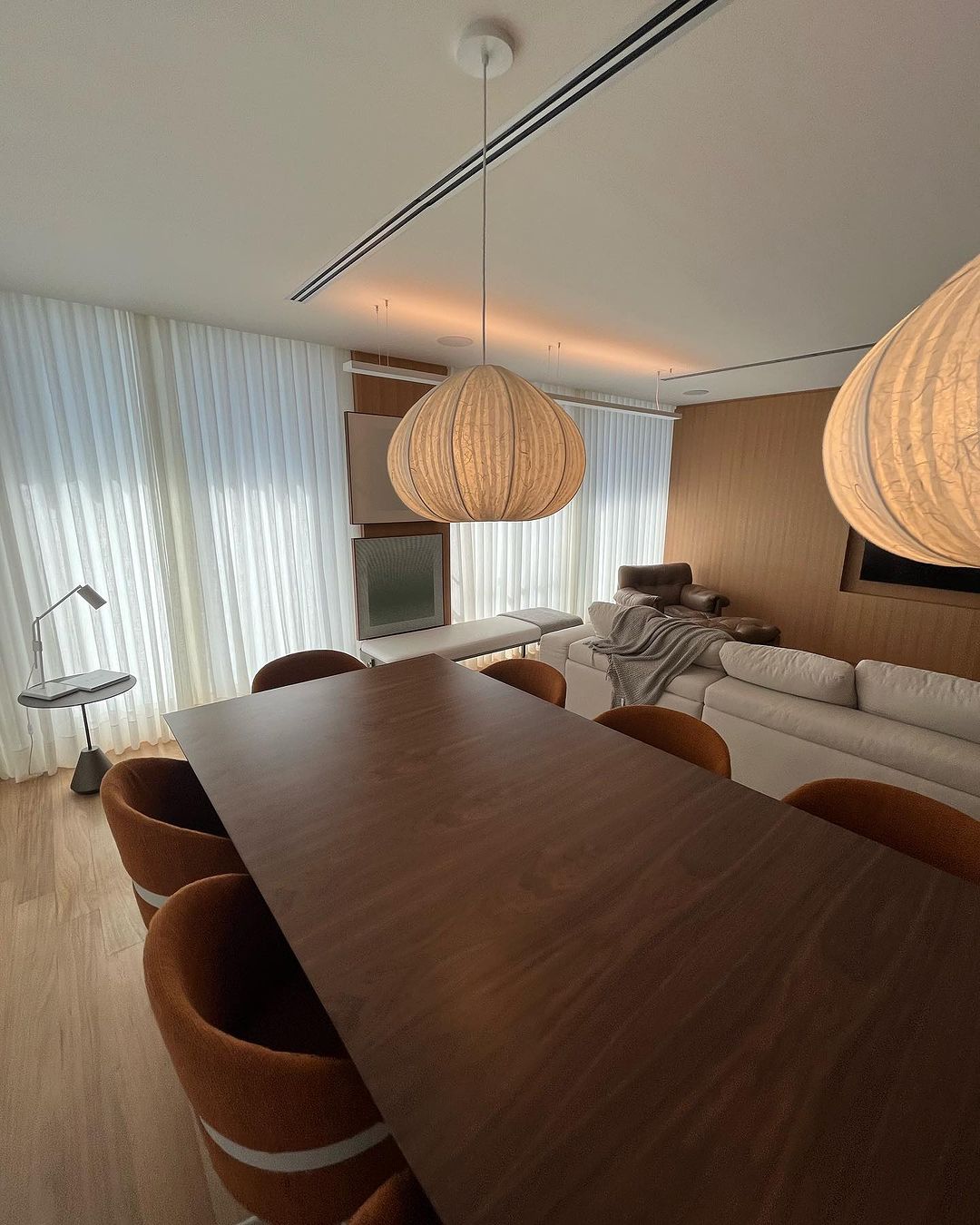 Cortinas brancas em ambiente integrado com lustres de madeira