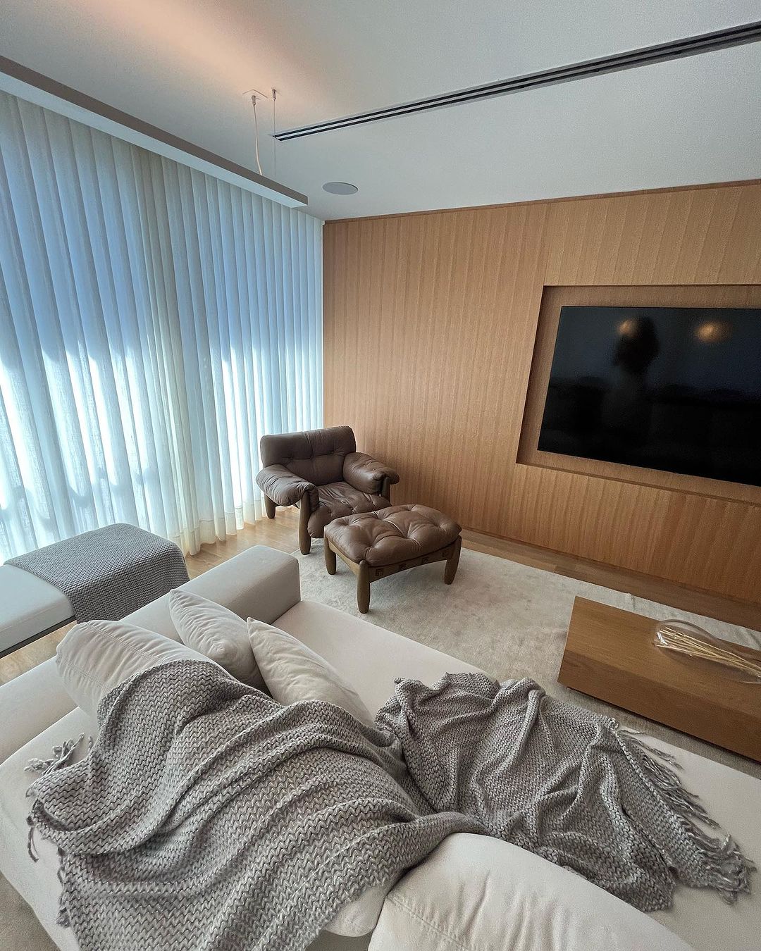 Cortinas verticais brancas em quarto com painel de madeira