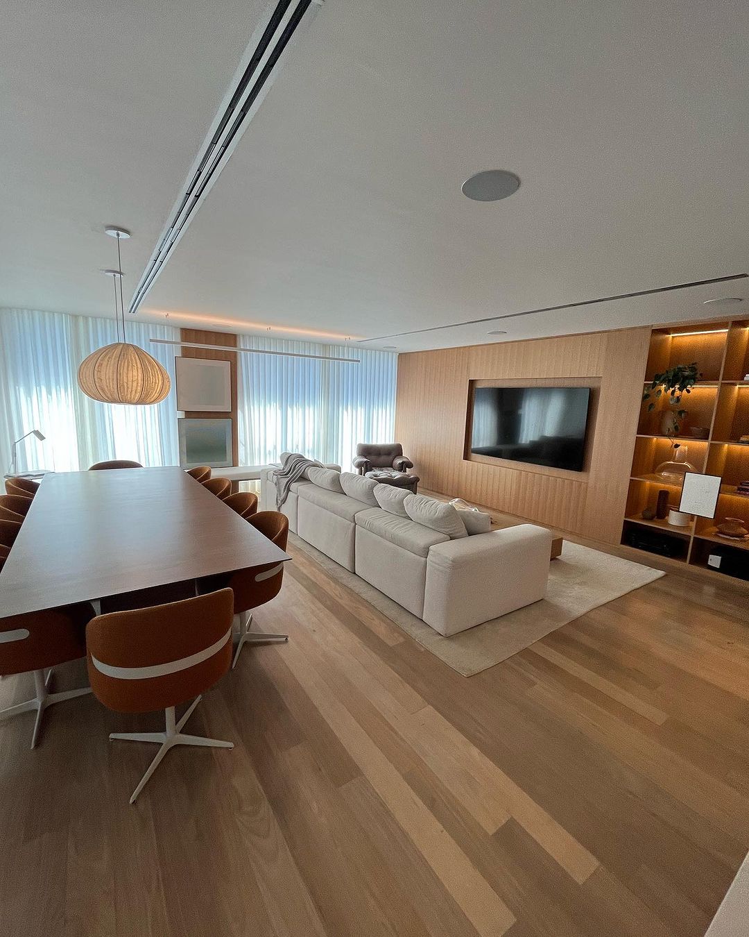 Cortinas brancas em sala de estar integrada com jantar e painel de madeira