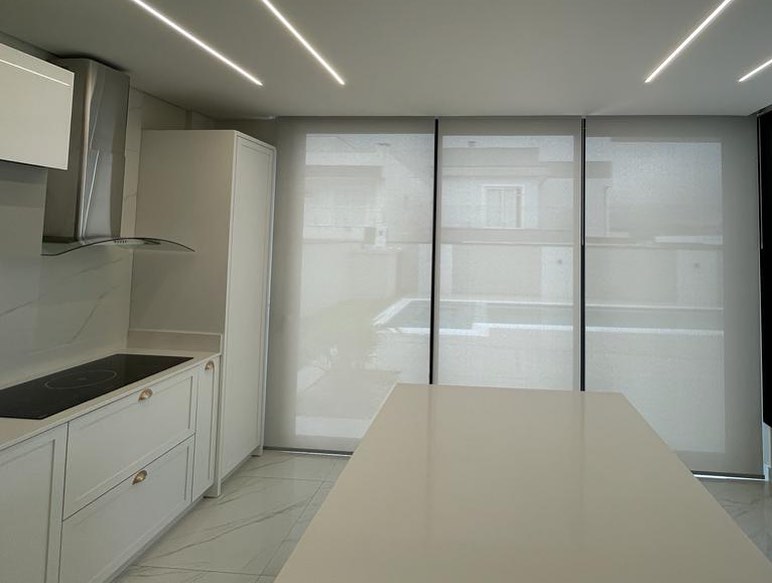 Persianas rolô brancas em painéis triplos em cozinha clara e moderna