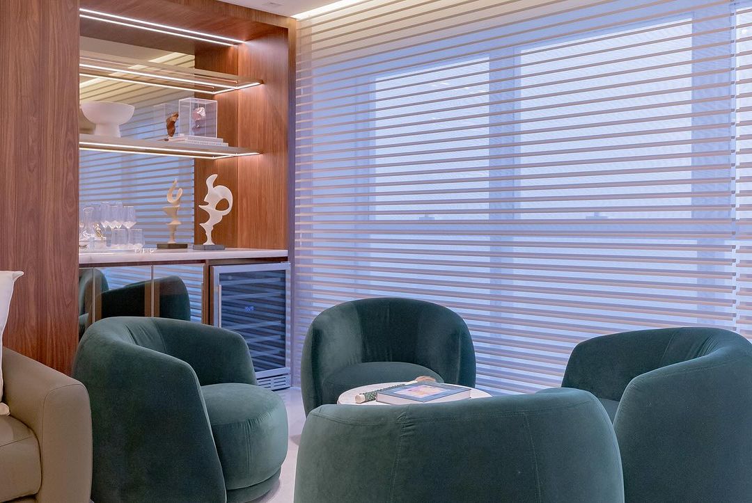 Persianas brancas horizontais em sala de estar com poltronas verdes