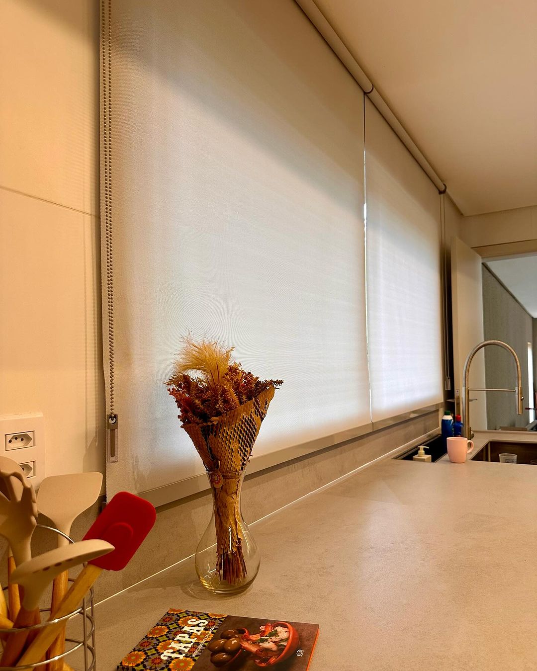 Cozinha aconchegante com persiana rolô bege e vaso com flores secas