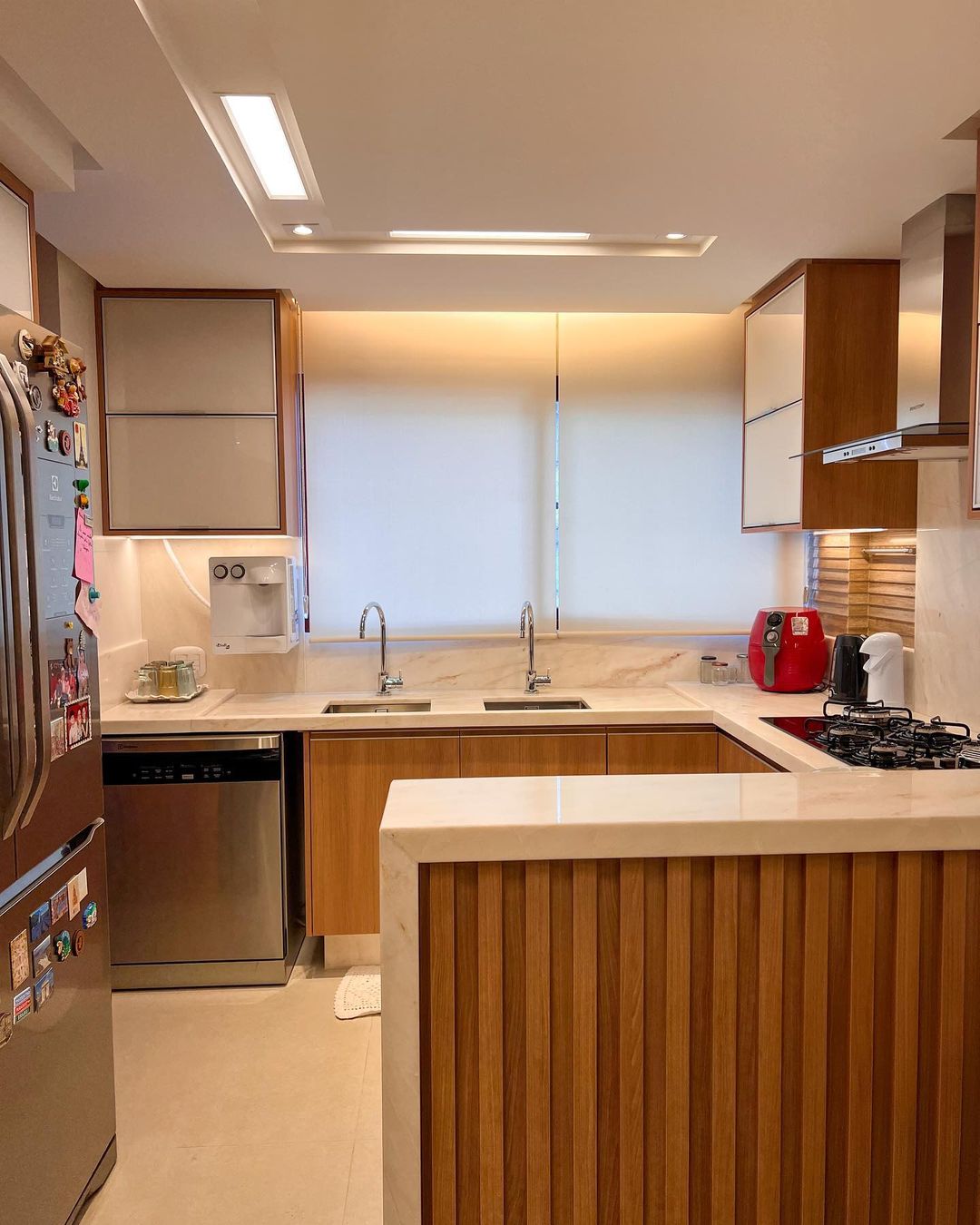 Cozinha planejada com persianas rolô brancas e armários de madeira