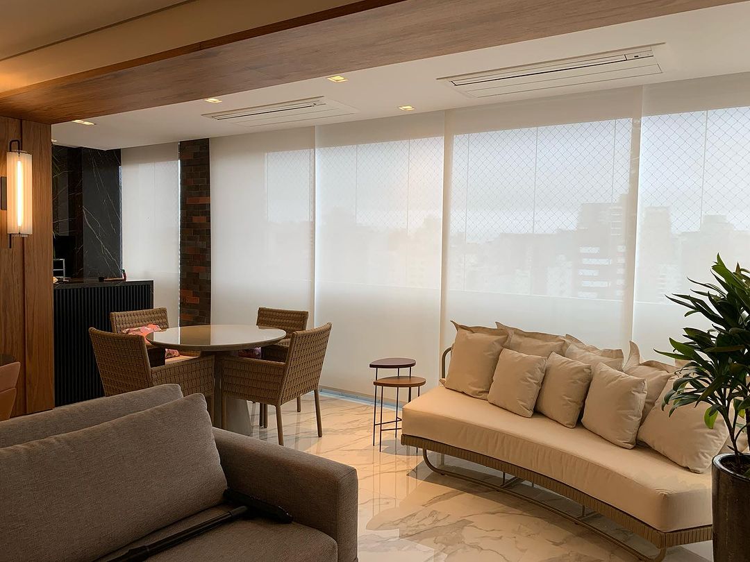 Varanda e sala de estar com persianas rolô brancas e sofás bege