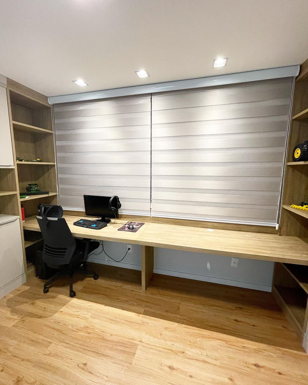 Home office moderno com persiana zebra cinza e bancada de madeira extensa