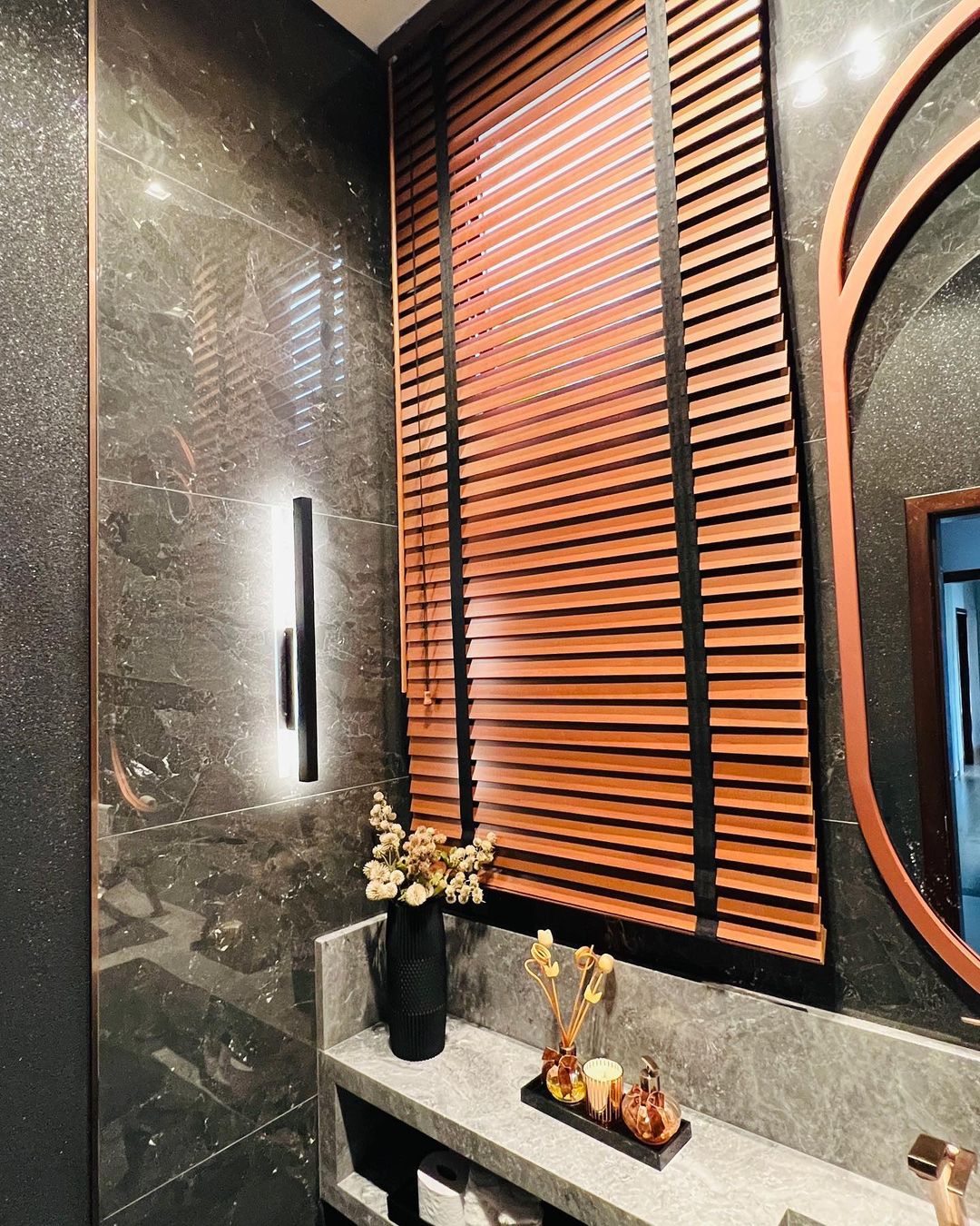 Persianas de madeira em lavabo sofisticado com mármore escuro